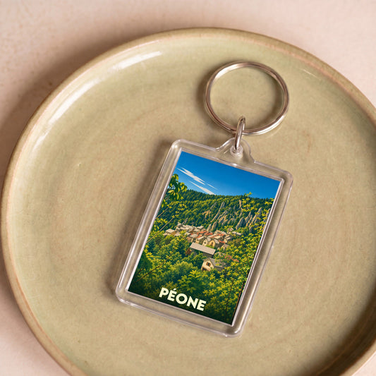 Porte-clés souvenir de la ville de Péone avec une illustration stylisée de son village niché dans la montagne.