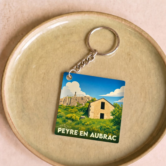 Porte-clés souvenir de la ville de Peyre en Aubrac avec une illustration stylisée d'un paysage local.