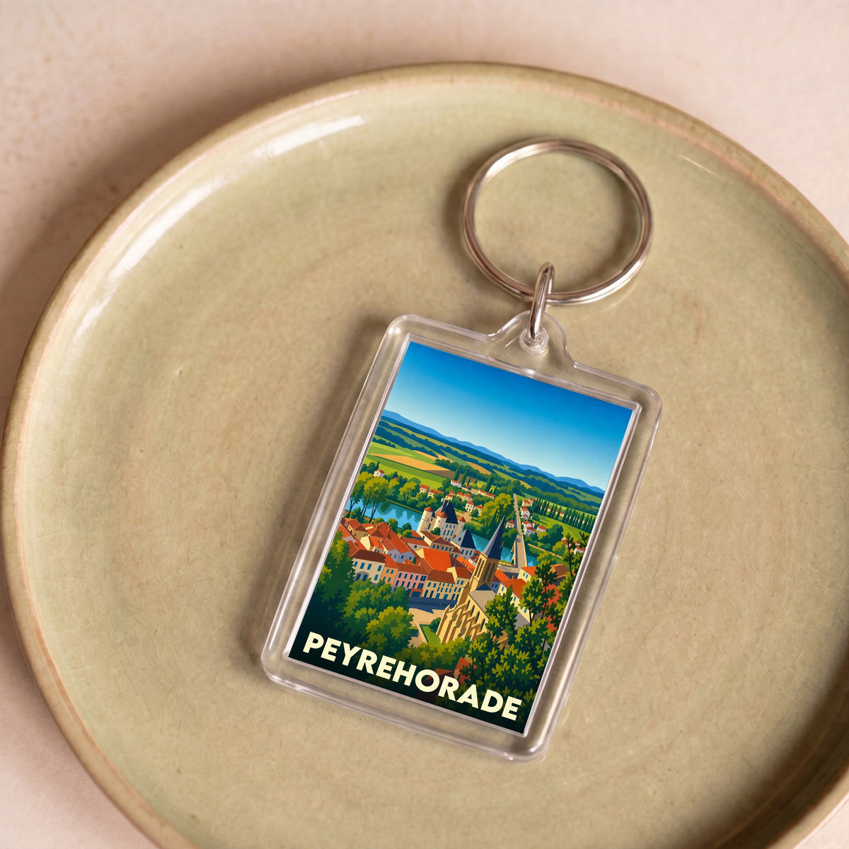 Porte-clés souvenir de la ville de Peyrehorade avec une illustration colorée et stylisée de son paysage.