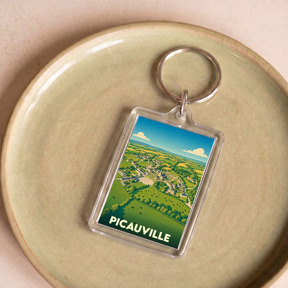 Porte-clés souvenir de la ville de Picauville avec une illustration stylisée de son paysage rural.