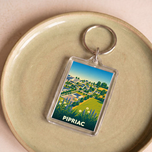 Porte-clés souvenir de la ville de Pipriac avec une illustration stylisée d'un paysage urbain et champêtre.