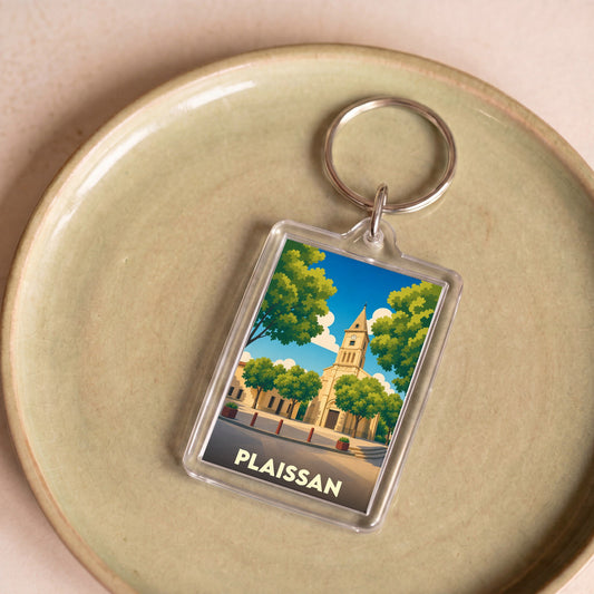 Porte-clés souvenir de la ville de Plaissan avec une illustration stylisée d'une église sous un ciel bleu.