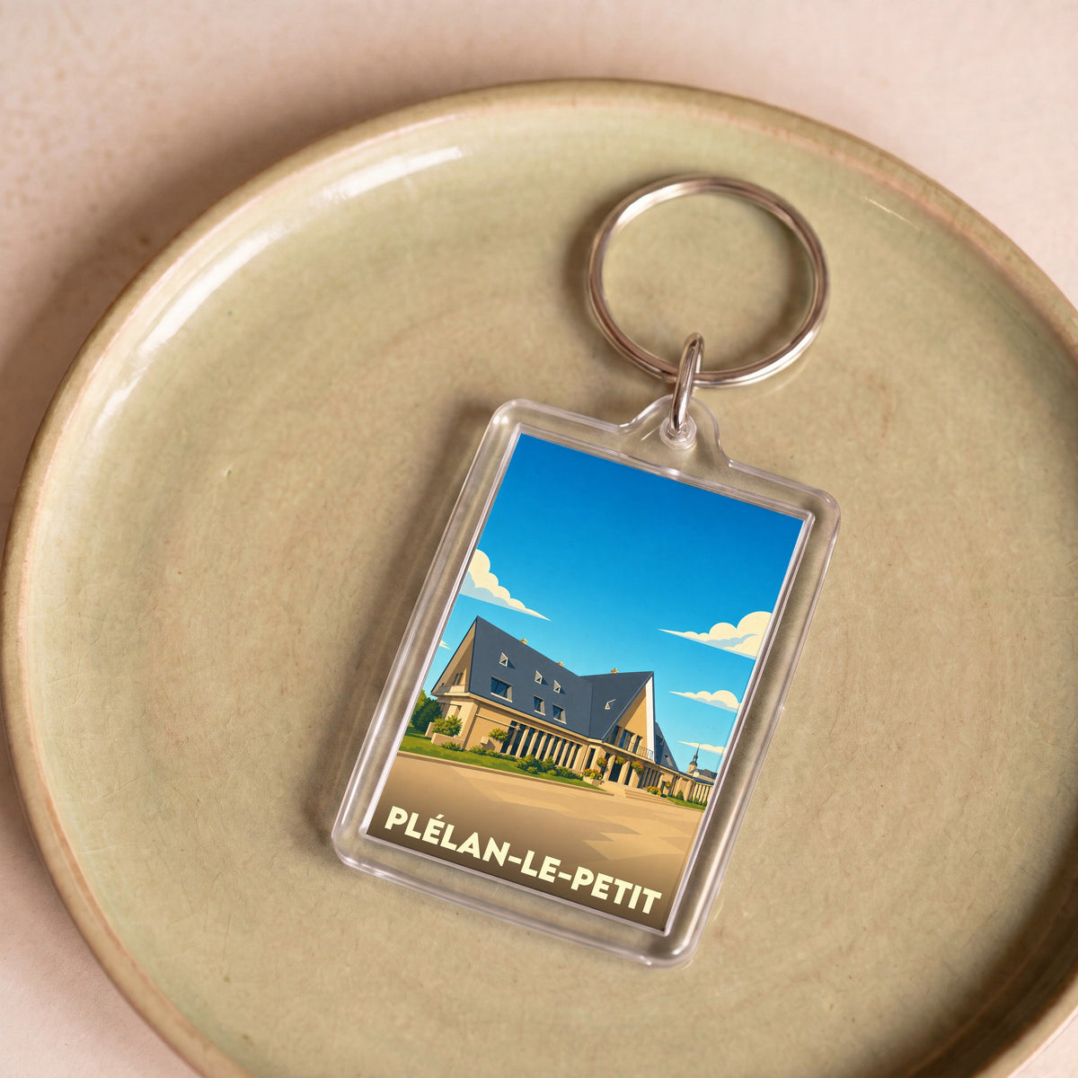 Porte-clés souvenir de la ville de Plélan-le-Petit avec une illustration stylisée.