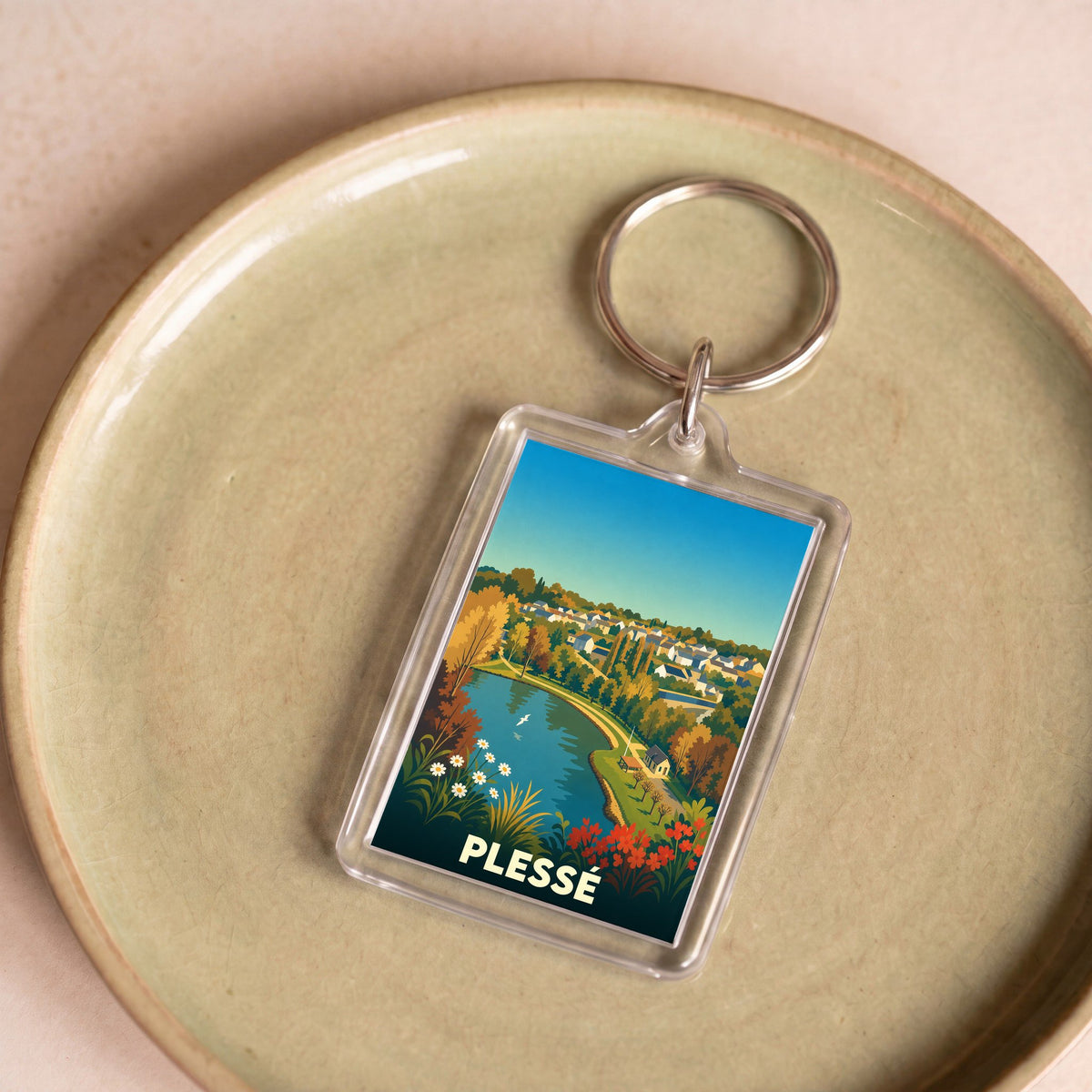 Porte-clés souvenir de la ville de Plessé avec une illustration stylisée d'un paysage local.