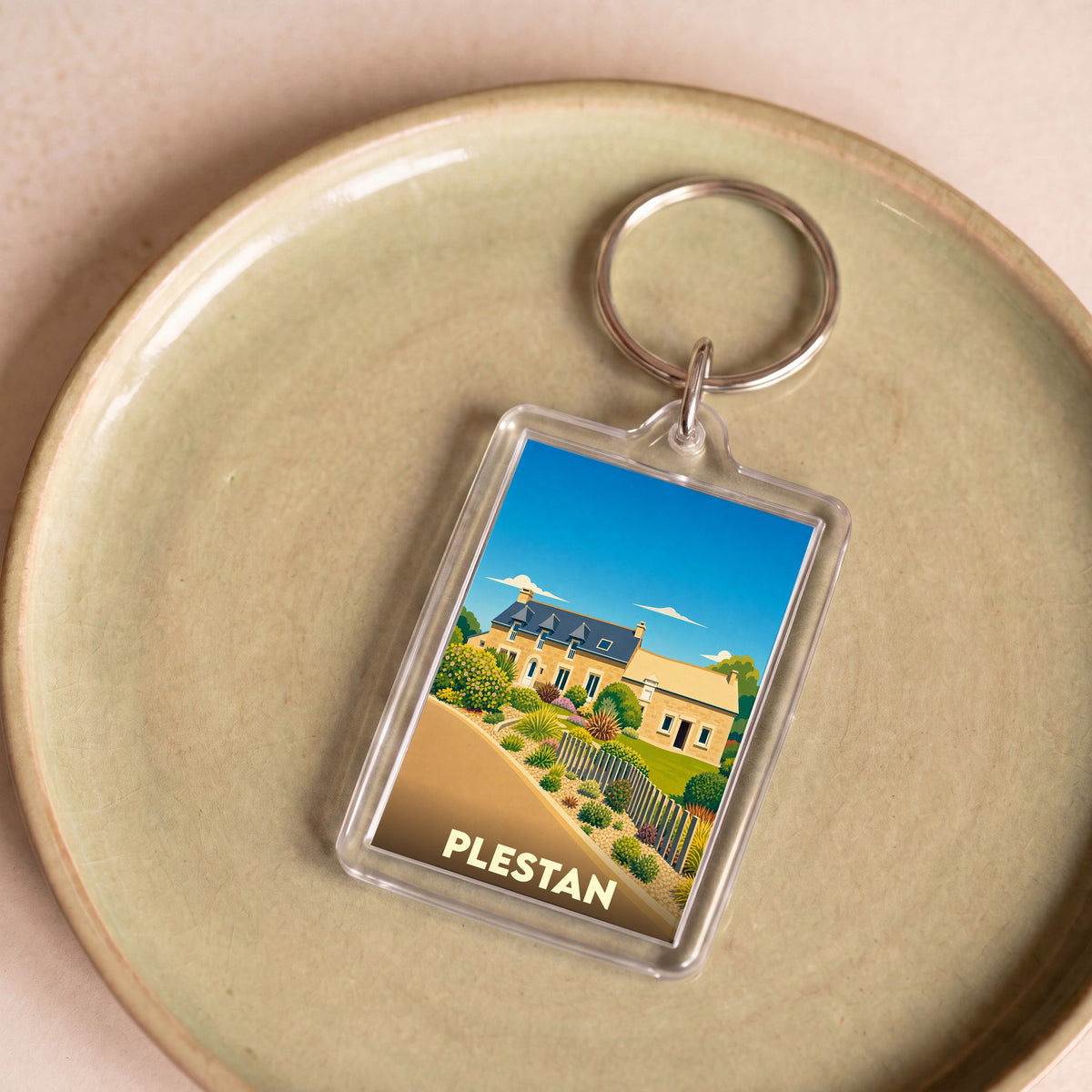 Porte-clés souvenir de la ville de Plestan avec une illustration stylisée d'une maison traditionnelle.