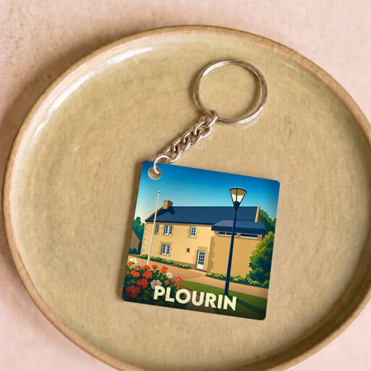 Porte-clés souvenir de la ville de Plourin avec une illustration stylisée d'un bâtiment breton fleuri.