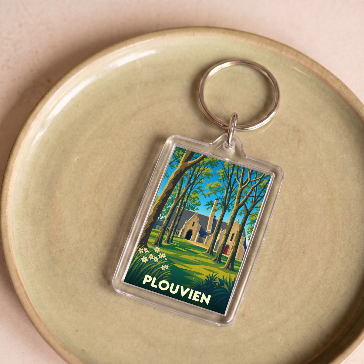Porte-clés souvenir de la ville de Plouvien avec une illustration stylisée d'une église sous les arbres.