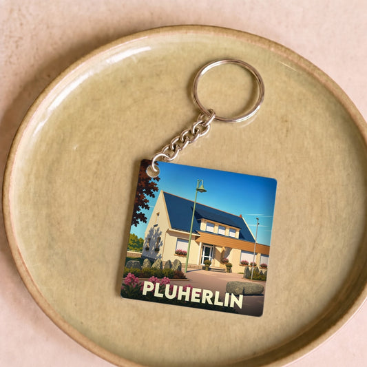 Porte-clés souvenir de la ville de Pluherlin avec une illustration stylisée d'une maison.