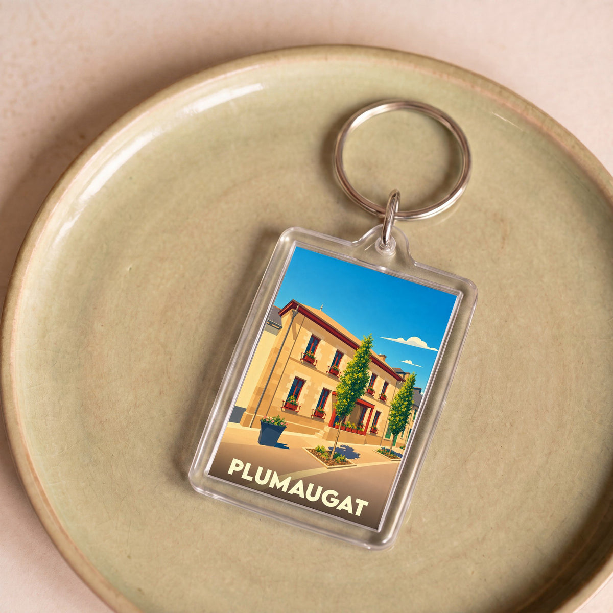 Porte-clés souvenir de la ville de Plumaugat avec une illustration stylisée d'un bâtiment fleuri.
