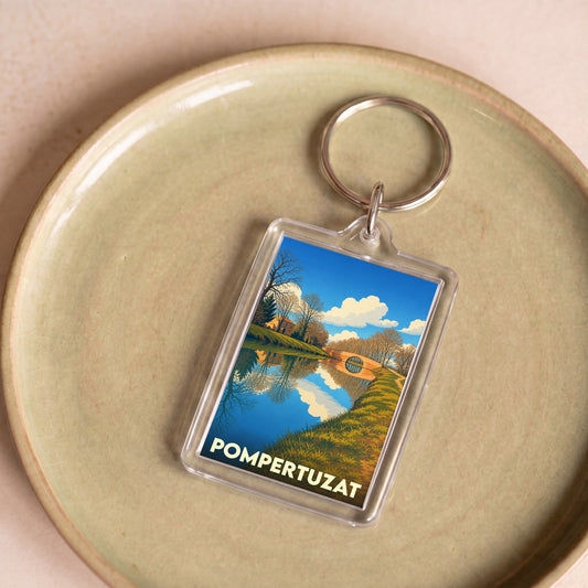 Porte-clés souvenir de la ville de Pompertuzat avec une illustration stylisée d'un paysage de canal.