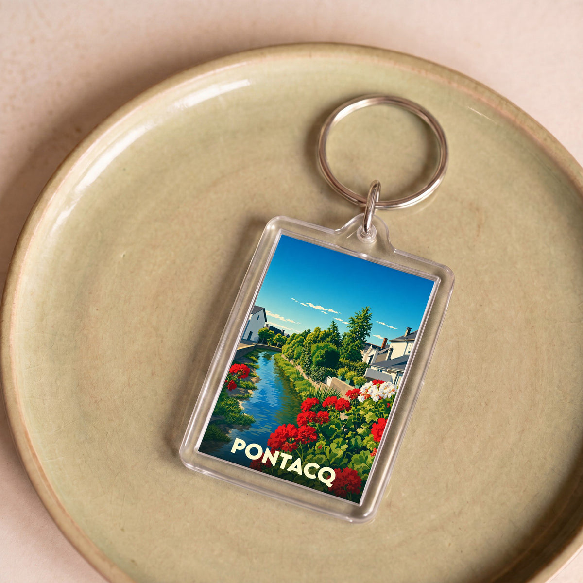 Porte-clés souvenir de la ville de Pontacq avec une illustration stylisée d'un canal fleuri.