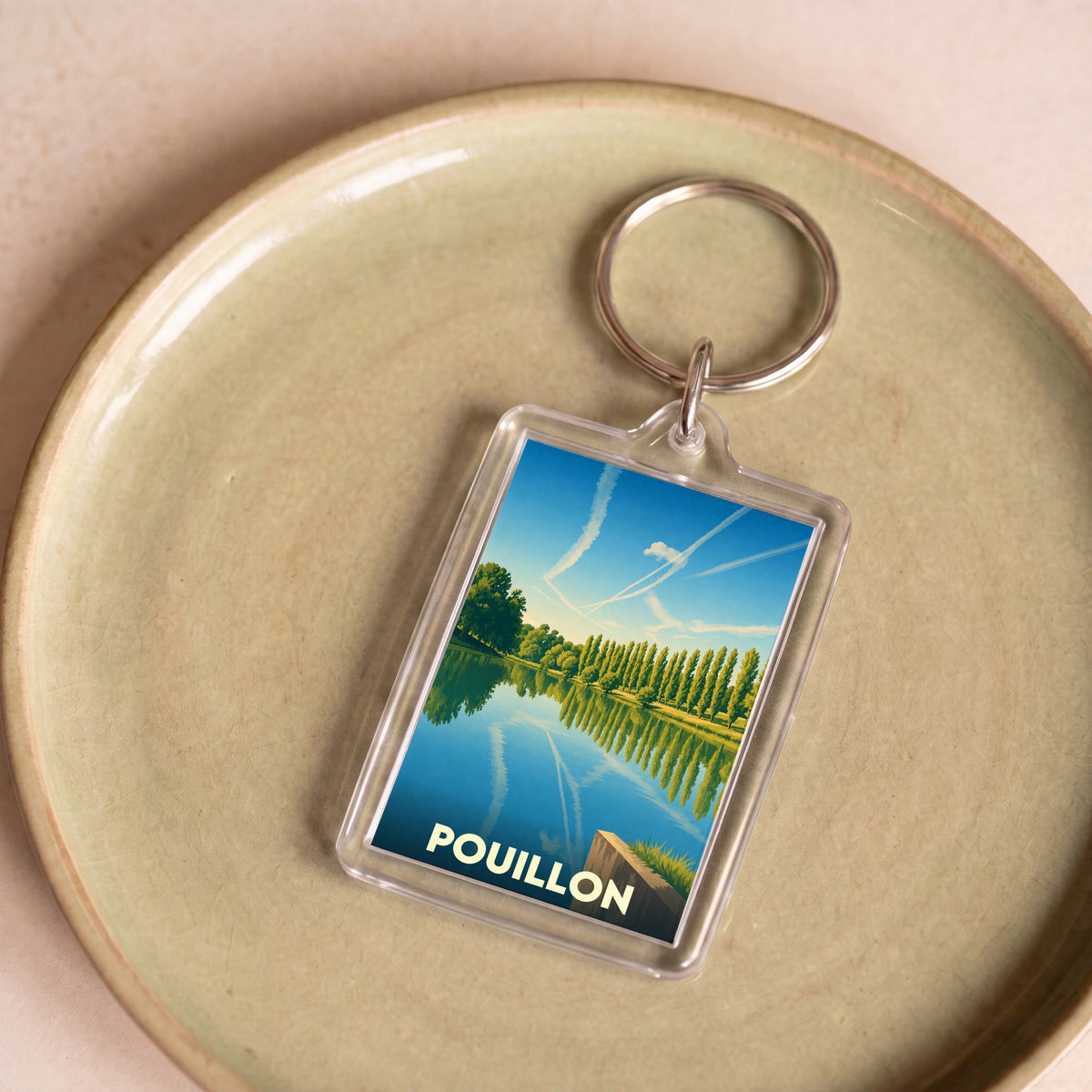 Porte-clés souvenir de la ville de Pouillon avec une illustration stylisée d'un lac bordé d'arbres.