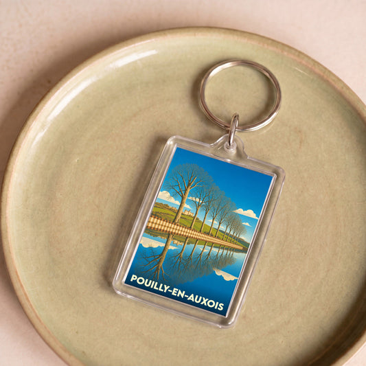 Porte-clés souvenir de Pouilly-en-Auxois illustrant une allée d'arbres se reflétant dans l'eau.