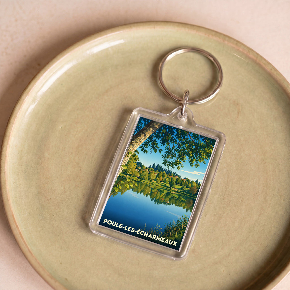Porte-clés souvenir de Poule-les-Écharmeaux avec une illustration stylisée d'un lac bordé de forêt.