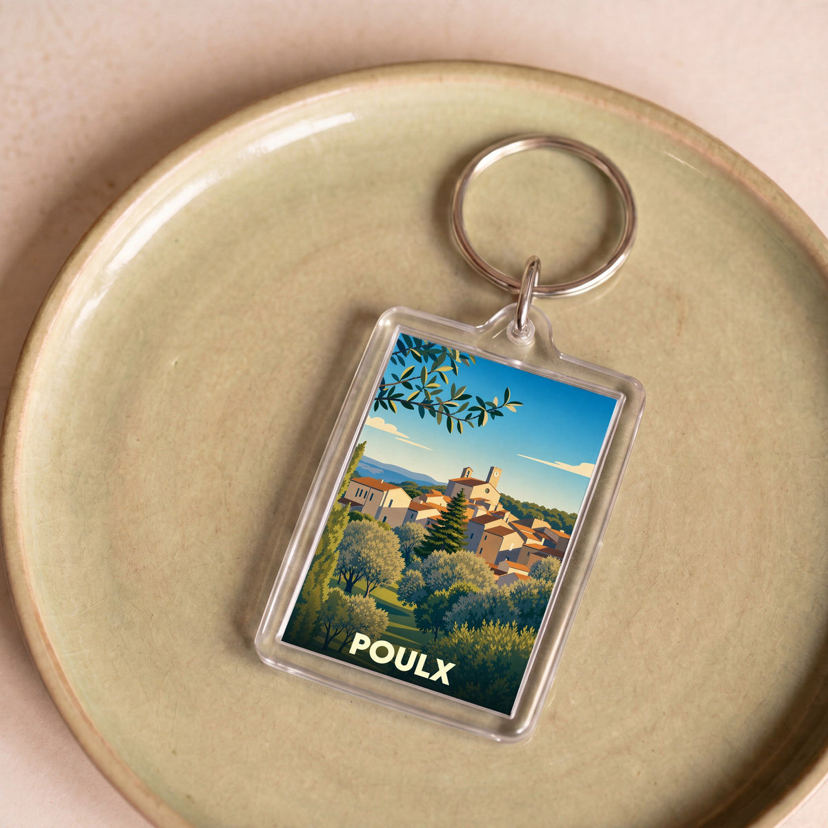 Porte-clés souvenir de la ville de Poulx avec une illustration stylisée d'un village provençal.