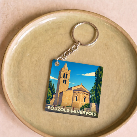 Porte-clés souvenir de la ville de Pouzols-Minervois avec une illustration stylisée de son église romane.