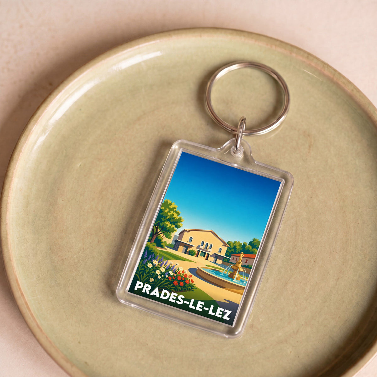 Porte-clés souvenir de la ville de Prades-le-Lez avec une illustration stylisée d'une place ensoleillée.