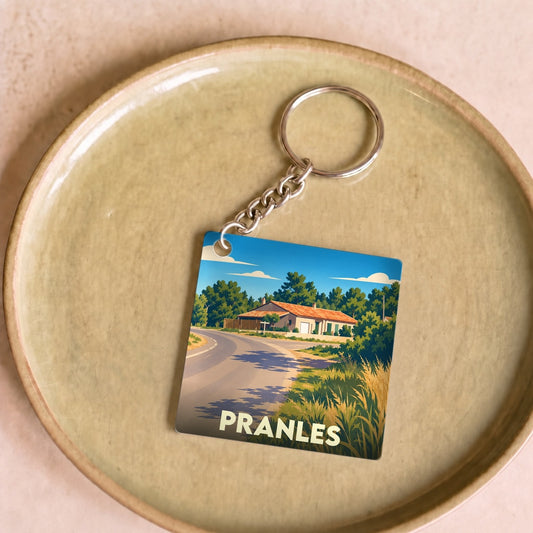 Porte-clés souvenir de la ville de Pranles avec une illustration stylisée d'un paysage de campagne.