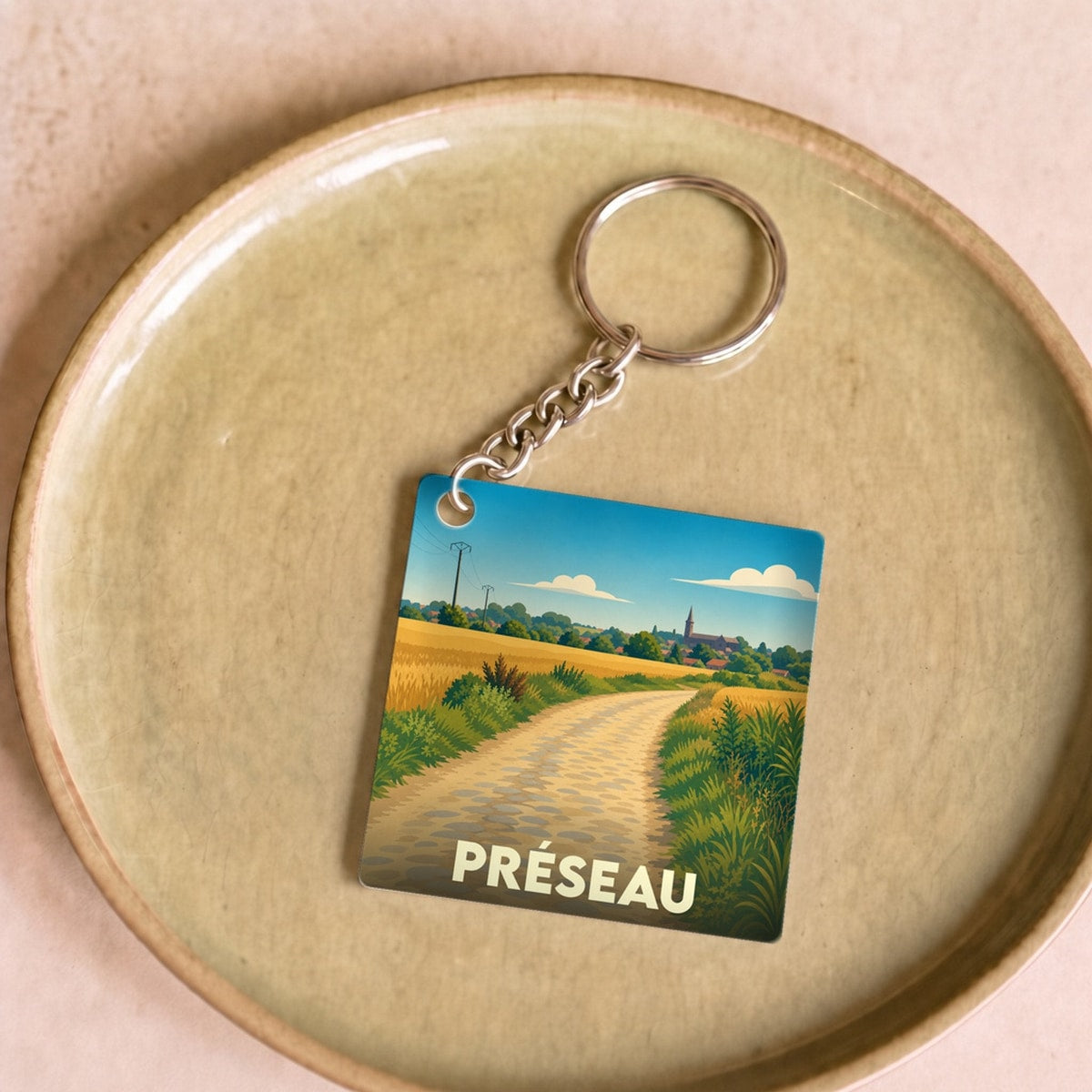 Porte-clés souvenir de la ville de Préseau avec une illustration stylisée d'un paysage champêtre.
