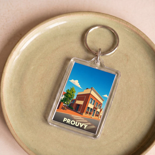 Porte-clés souvenir de la ville de Prouvy avec une illustration stylisée d'un bâtiment urbain sous un ciel bleu.