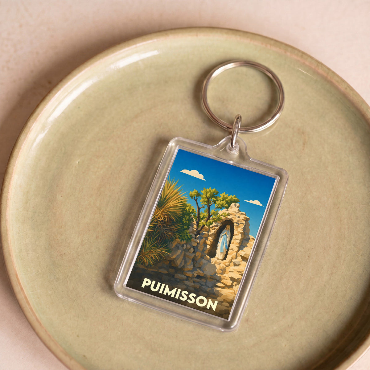 Porte-clés souvenir de la ville de Puimisson avec une illustration stylisée d'une statue dans une grotte de pierre.