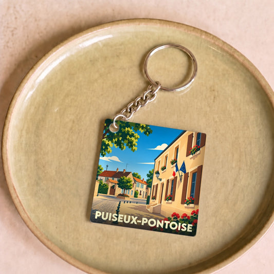 Porte-clés souvenir de la ville de Puiseux-Pontoise avec une illustration stylisée d'une rue ensoleillée.