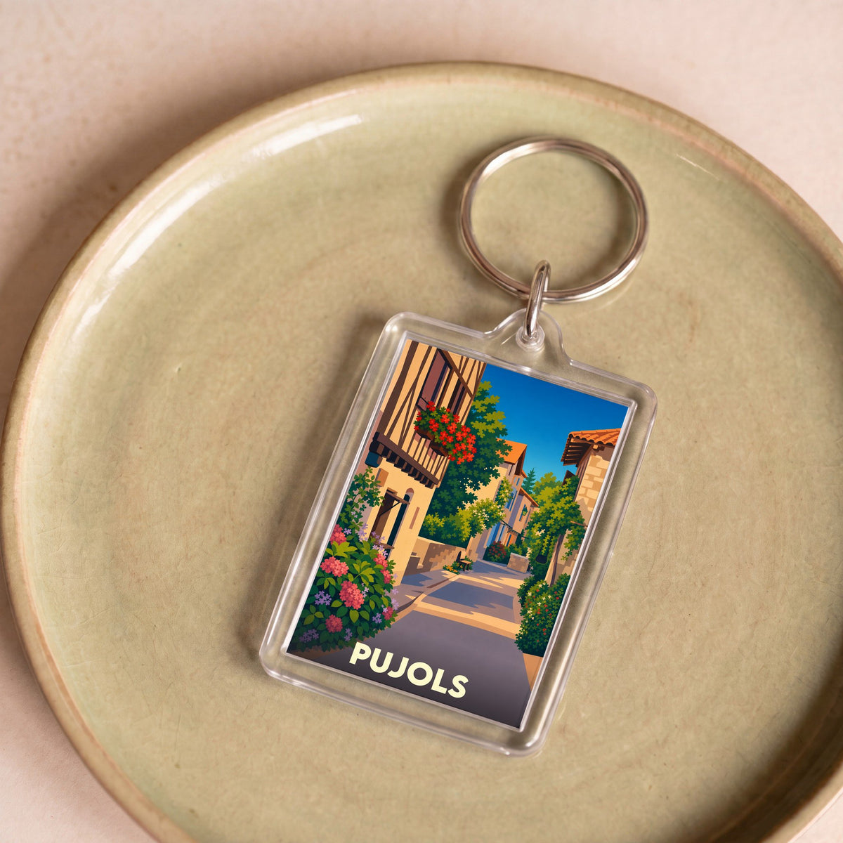 Porte-clés souvenir de la ville de Pujols avec une illustration stylisée d'une ruelle fleurie.