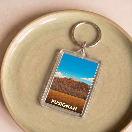 Porte-clés souvenir de la ville de Pusignan avec une illustration stylisée d'un paysage automnal.