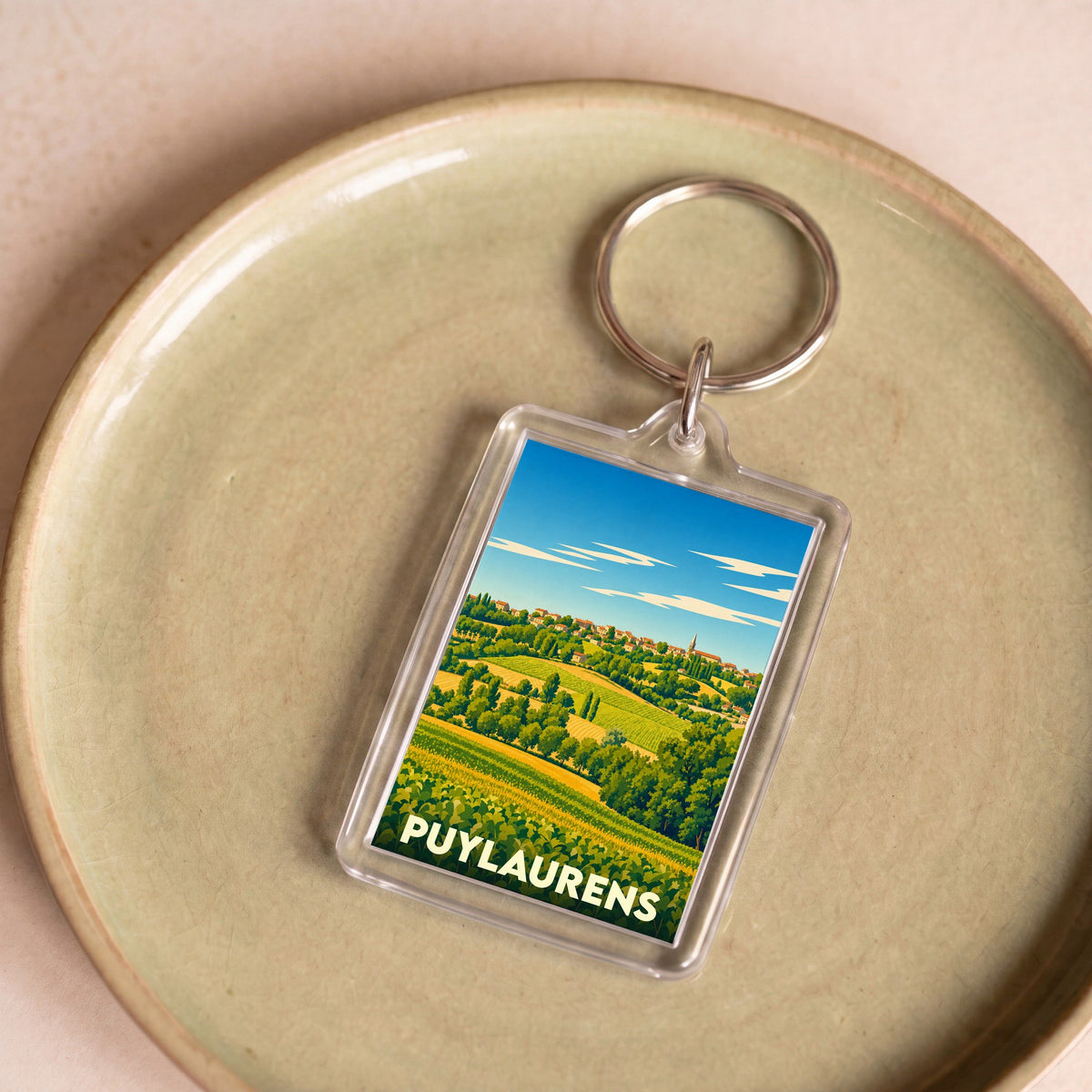 Porte-clés souvenir de la ville de Puylaurens avec une illustration stylisée de son paysage vallonné.