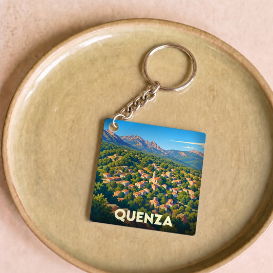Porte-clés souvenir de la ville de Quenza avec une illustration stylisée d'un village de montagne.