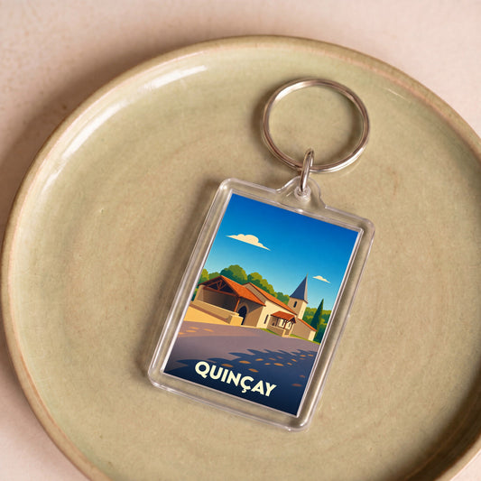 Porte-clés souvenir de la ville de Quinçay avec une illustration stylisée de son église et de ses bâtiments.