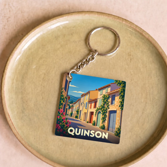 Porte-clés souvenir de la ville de Quinson avec une illustration stylisée d'une ruelle provençale colorée.