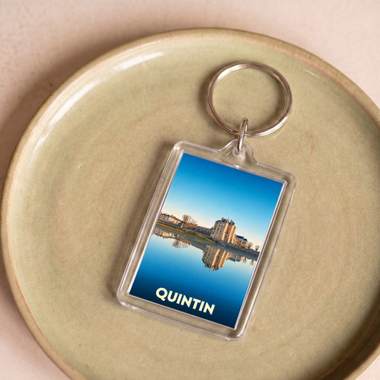 Porte-clés souvenir de la ville de Quintin illustré par une photographie du château se reflétant dans l'eau.