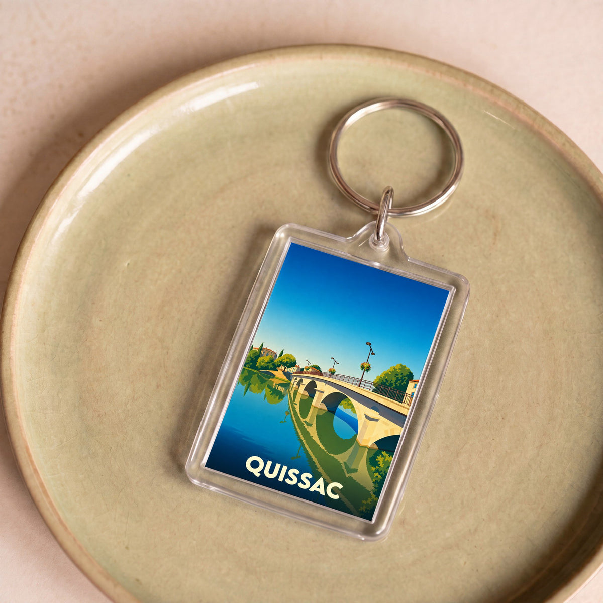 Porte-clés souvenir de la ville de Quissac avec une illustration stylisée de son pont.