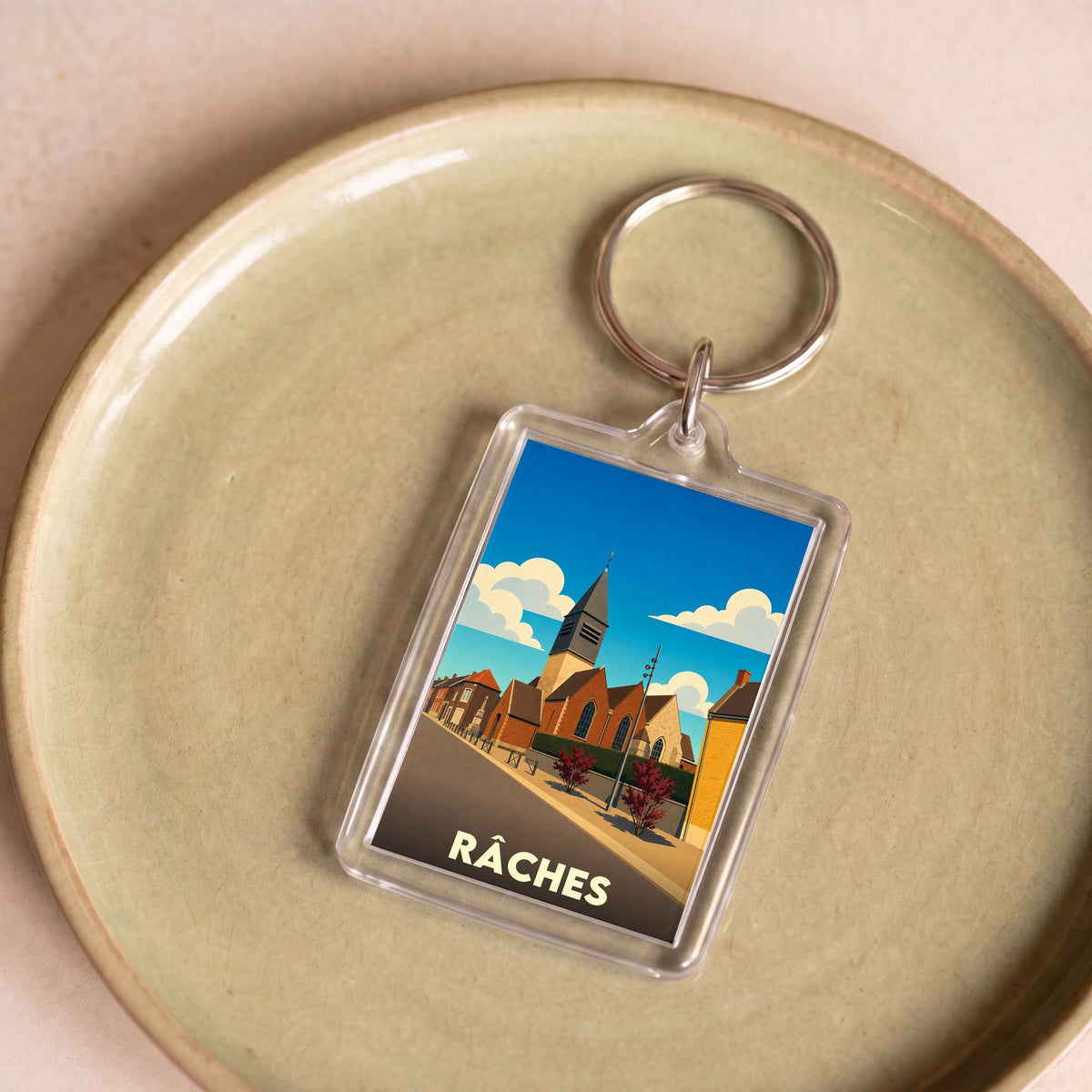 Porte-clés souvenir de la ville de Râches avec une illustration stylisée.
