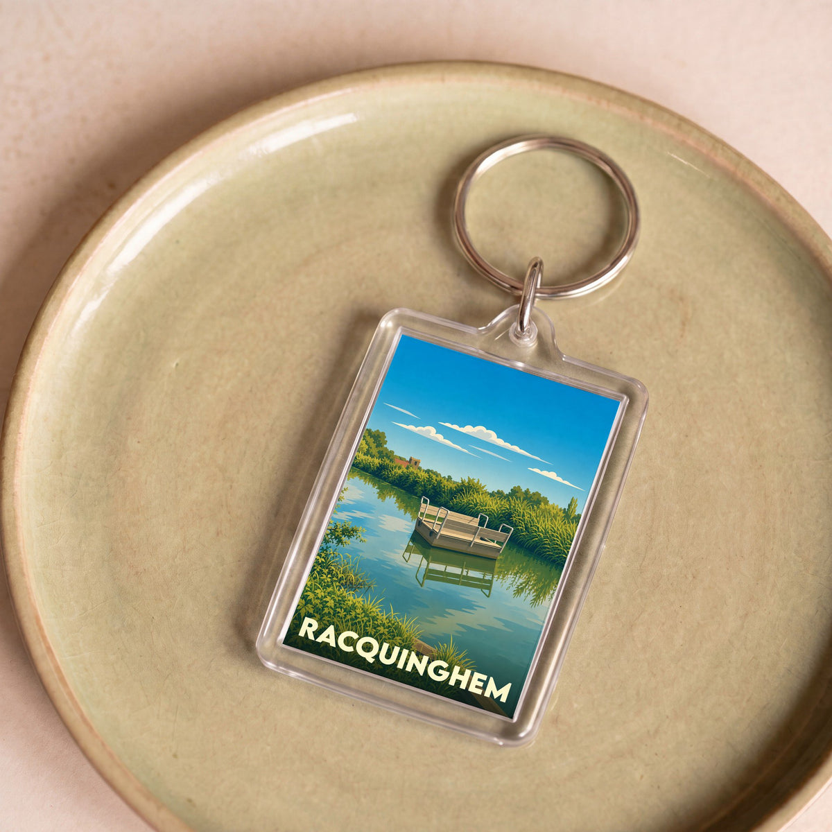 Porte-clés souvenir de la ville de Racquinghem avec une illustration stylisée d'un paysage fluvial.