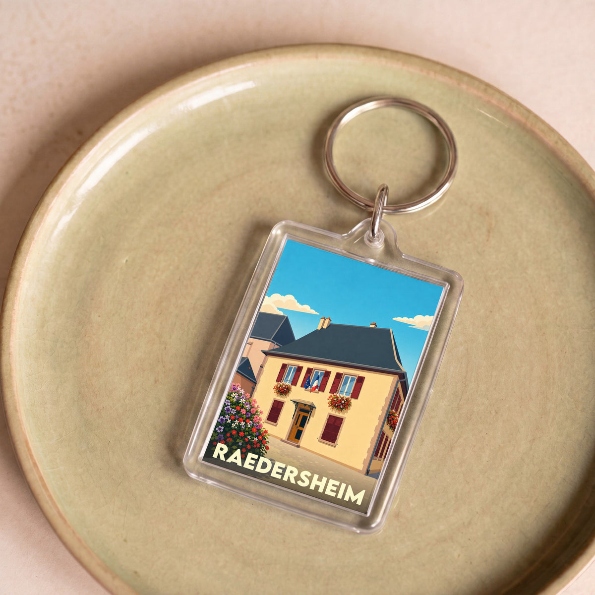 Porte-clés souvenir de la ville de Raedersheim avec une illustration stylisée de sa mairie fleurie.
