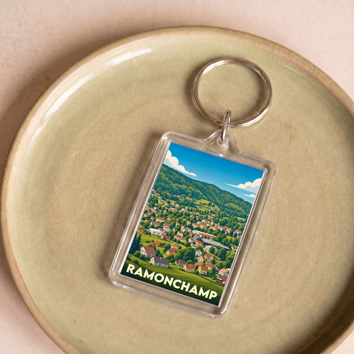 Porte-clés souvenir de la ville de Ramonchamp avec une illustration stylisée de son paysage montagneux.