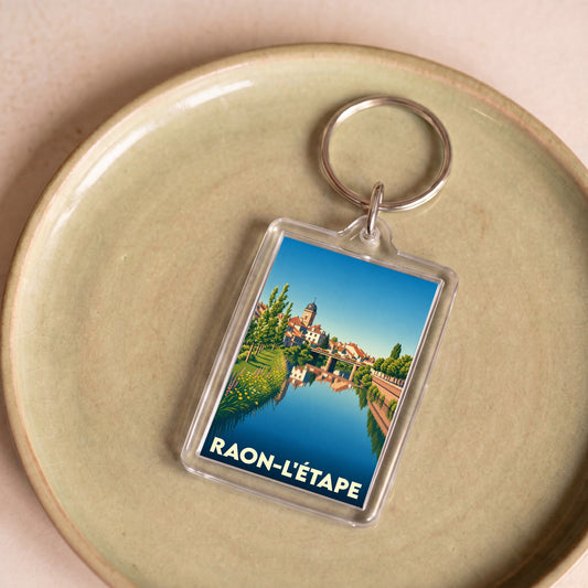 Porte-clés souvenir de la ville de Raon-l'Étape avec une illustration stylisée d'un paysage urbain au bord de l'eau.