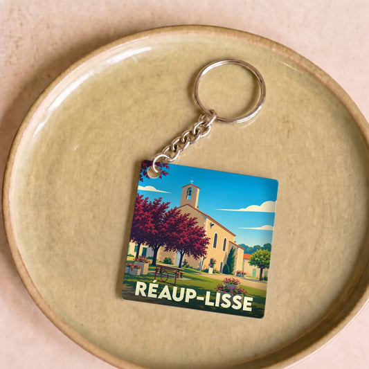 Porte-clés souvenir de la ville de Réaup-Lisse avec une illustration stylisée de son église et de paysages arborés.