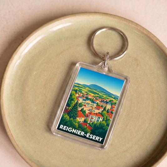 Porte-clés souvenir de la ville de Reignier-Ésery avec une illustration colorée et stylisée du paysage local.