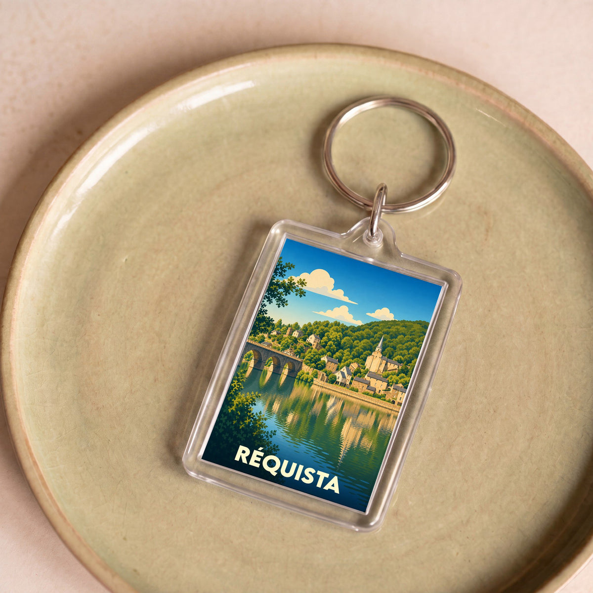 Porte-clés souvenir de la ville de Réquista avec une illustration stylisée d'un paysage fluvial.