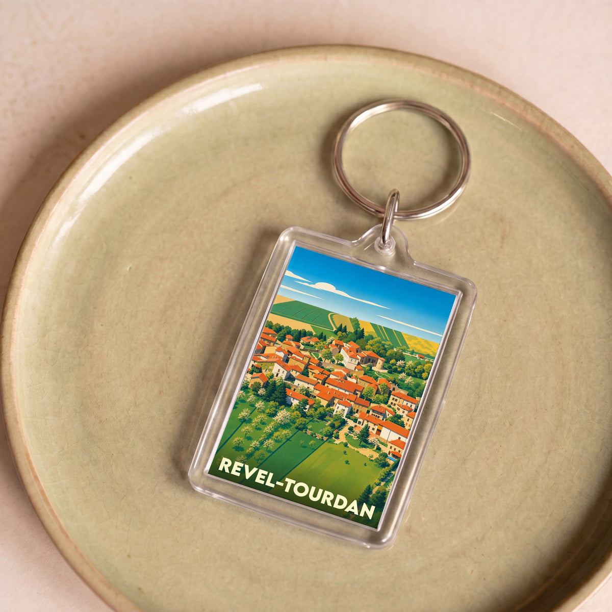 Porte-clés souvenir de la ville de Revel-Tourdan avec une illustration stylisée de ses paysages et toitures.