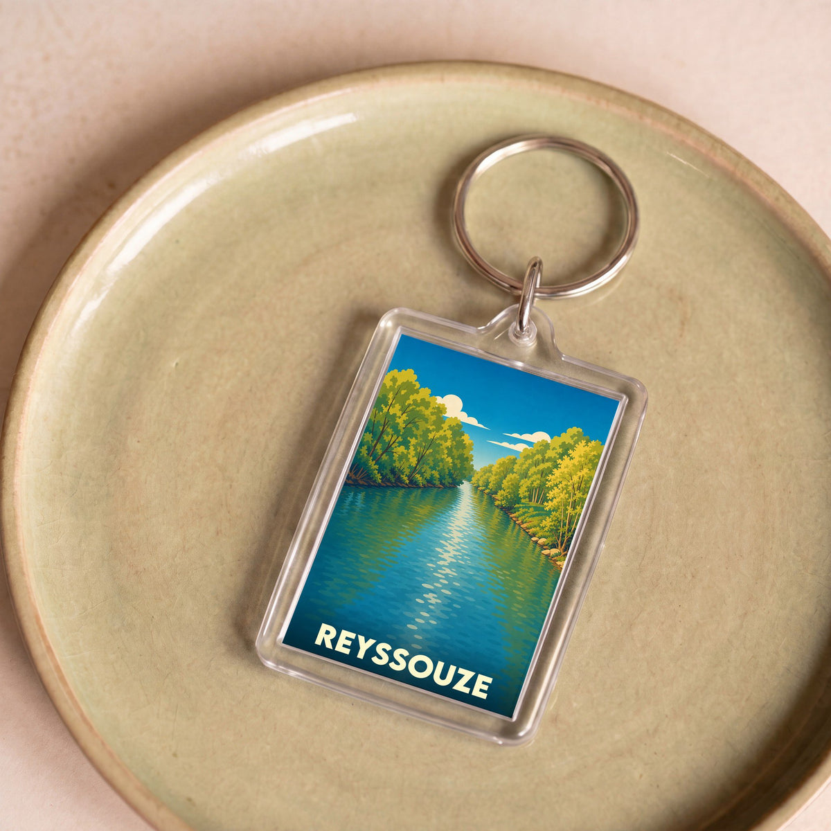 Porte-clés souvenir de la ville de Reyssouze avec une illustration stylisée d'une rivière bordée d'arbres.