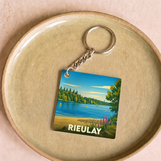 Porte-clés souvenir de la ville de Rieulay avec une illustration stylisée d'un paysage de lac.
