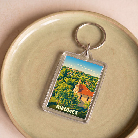 Porte-clés souvenir de la ville de Rieumes avec une illustration stylisée d'un paysage de campagne et de son église.
