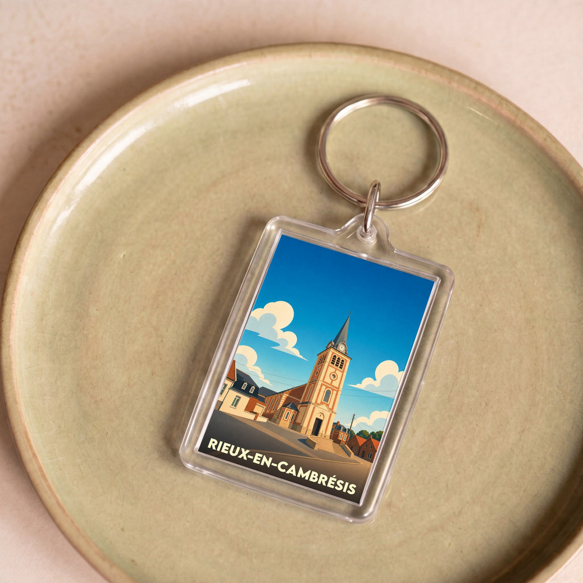 Porte-clés souvenir de la ville de Rieux-en-Cambrésis avec une illustration stylisée de son église sous un ciel bleu.