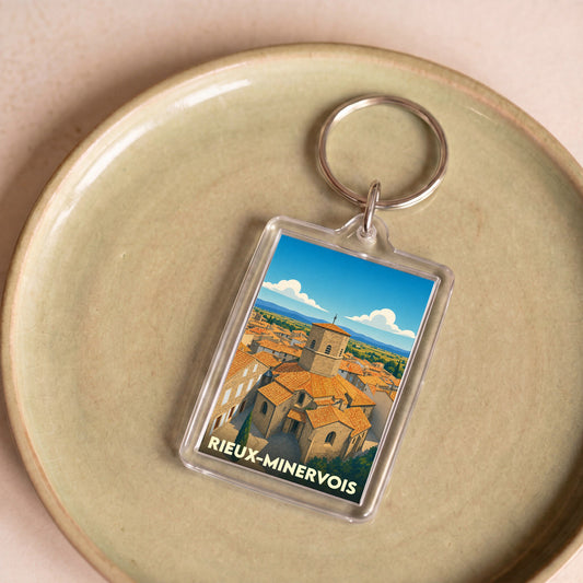 Porte-clés souvenir de la ville de Rieux-Minervois avec une illustration stylisée de son église et de ses toits.