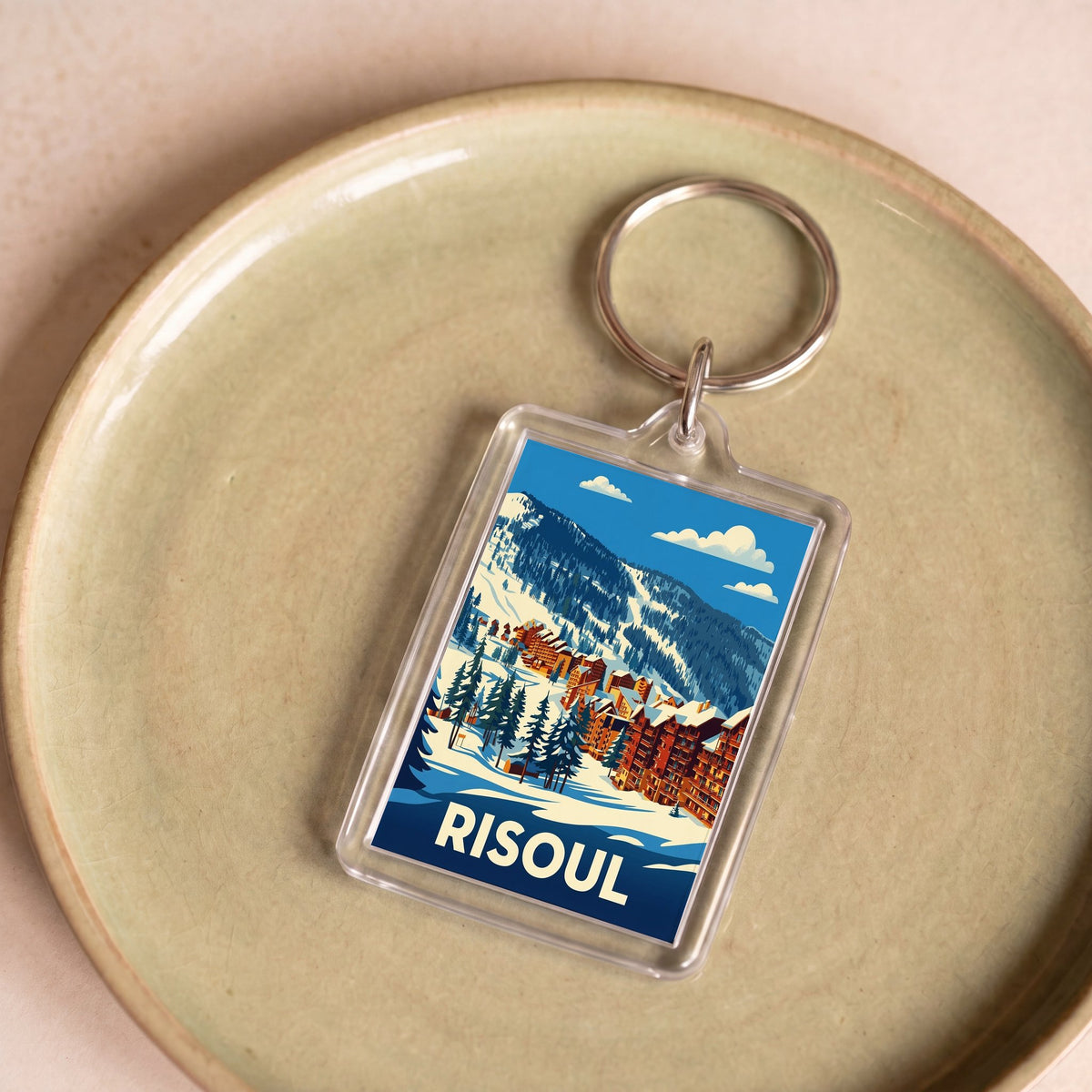 Porte-clés souvenir de la ville de Risoul avec une illustration stylisée de paysages enneigés.