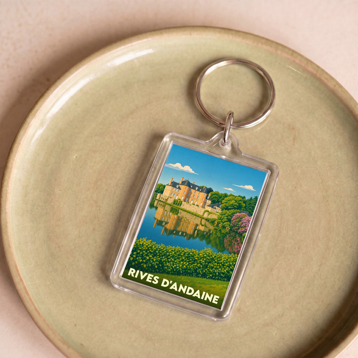 Porte-clés souvenir de la ville de Rives d'Andaine avec une illustration stylisée d'un château se reflétant dans l'eau.